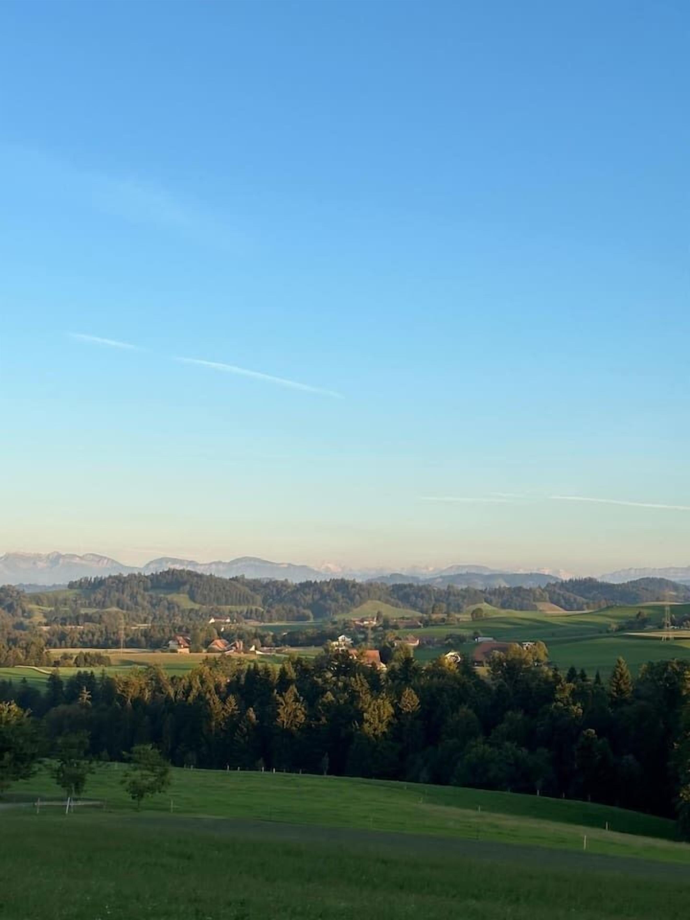 Un paysage rural caractérisé par un ciel dégagé, des collines ondoyantes et des bâtiments dispersés.
