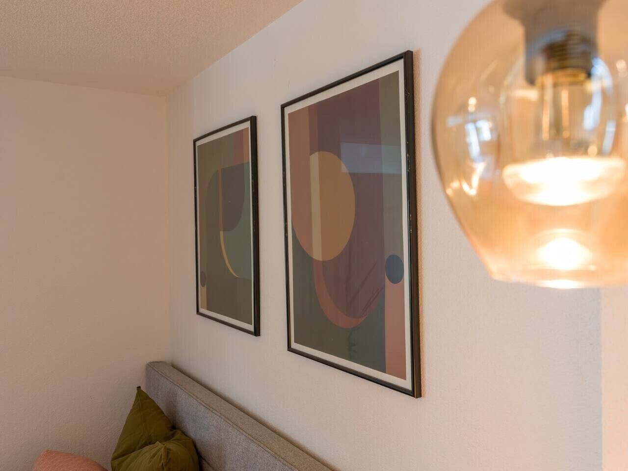 Ein Zimmer mit einem Bett, einer Wandleuchte und zwei gerahmten abstrakten Bildern.