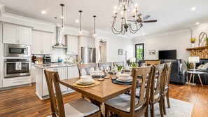 A modern kitchen with white cabinets, stainless steel appliances, and a dining area with a wooden table set for four. - Heated Saltwater Pool - 3BR Home - Gulfport (Gulfport)