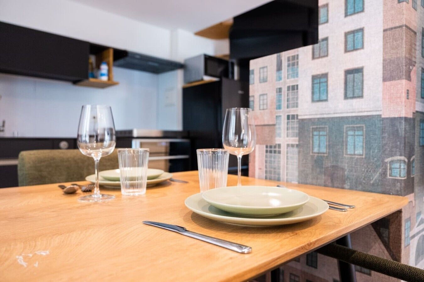 A dining table set with plates, glasses, and cutlery, with a cityscape mural in the background.