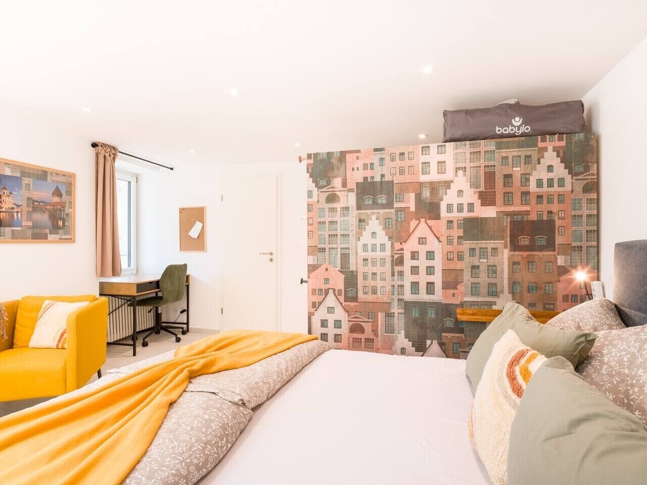 Habitación de hotel con cama, escritorio, silla y un mural de paisaje urbano.