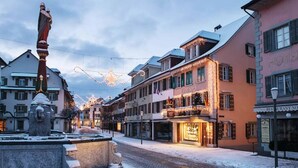 A snow-covered street with a fountain, buildings with shops, and a hotel.
