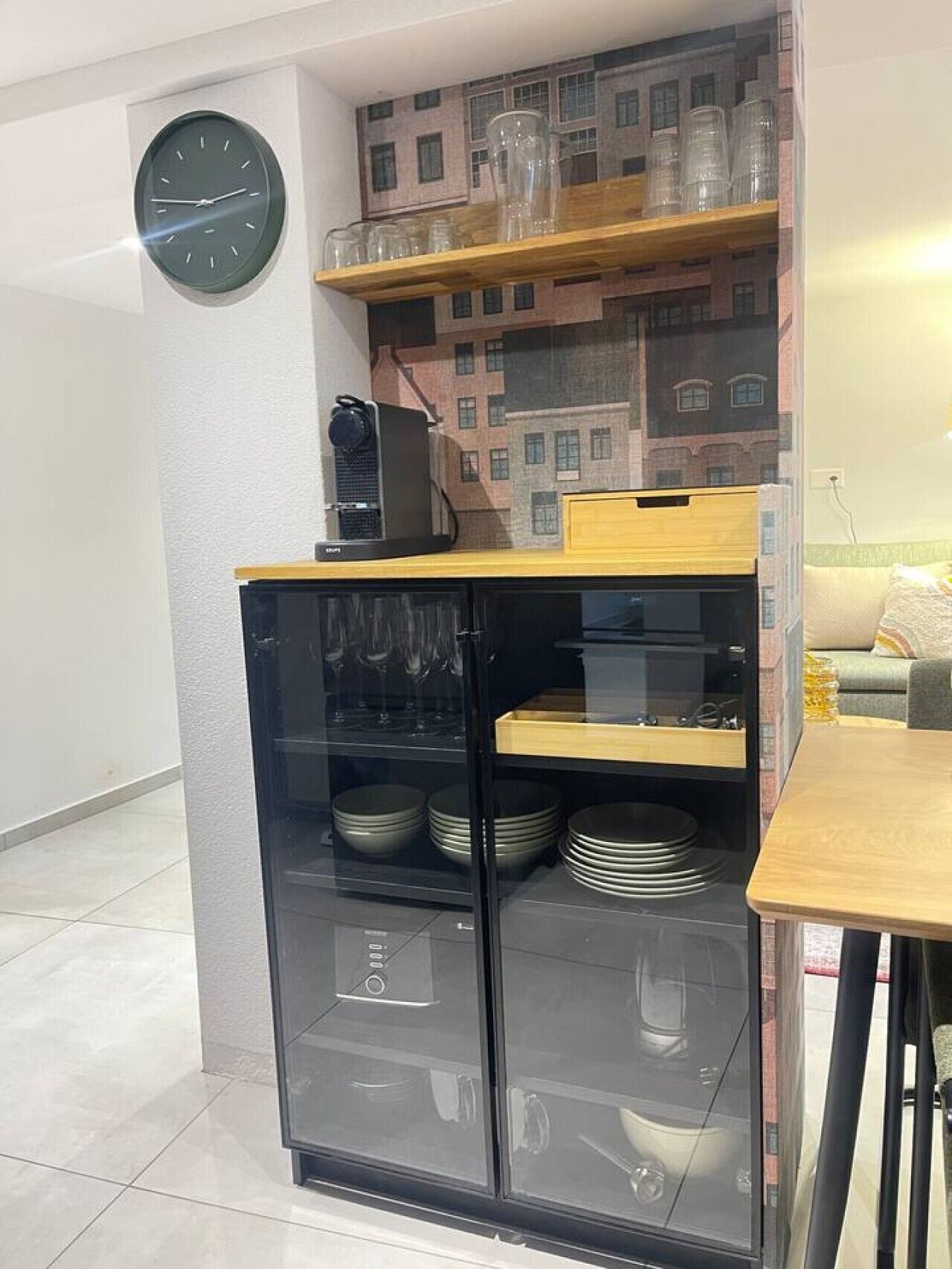 Une cuisine équipée d’un réfrigérateur encastré, d’une horloge au mur et d’un papier peint à motifs.