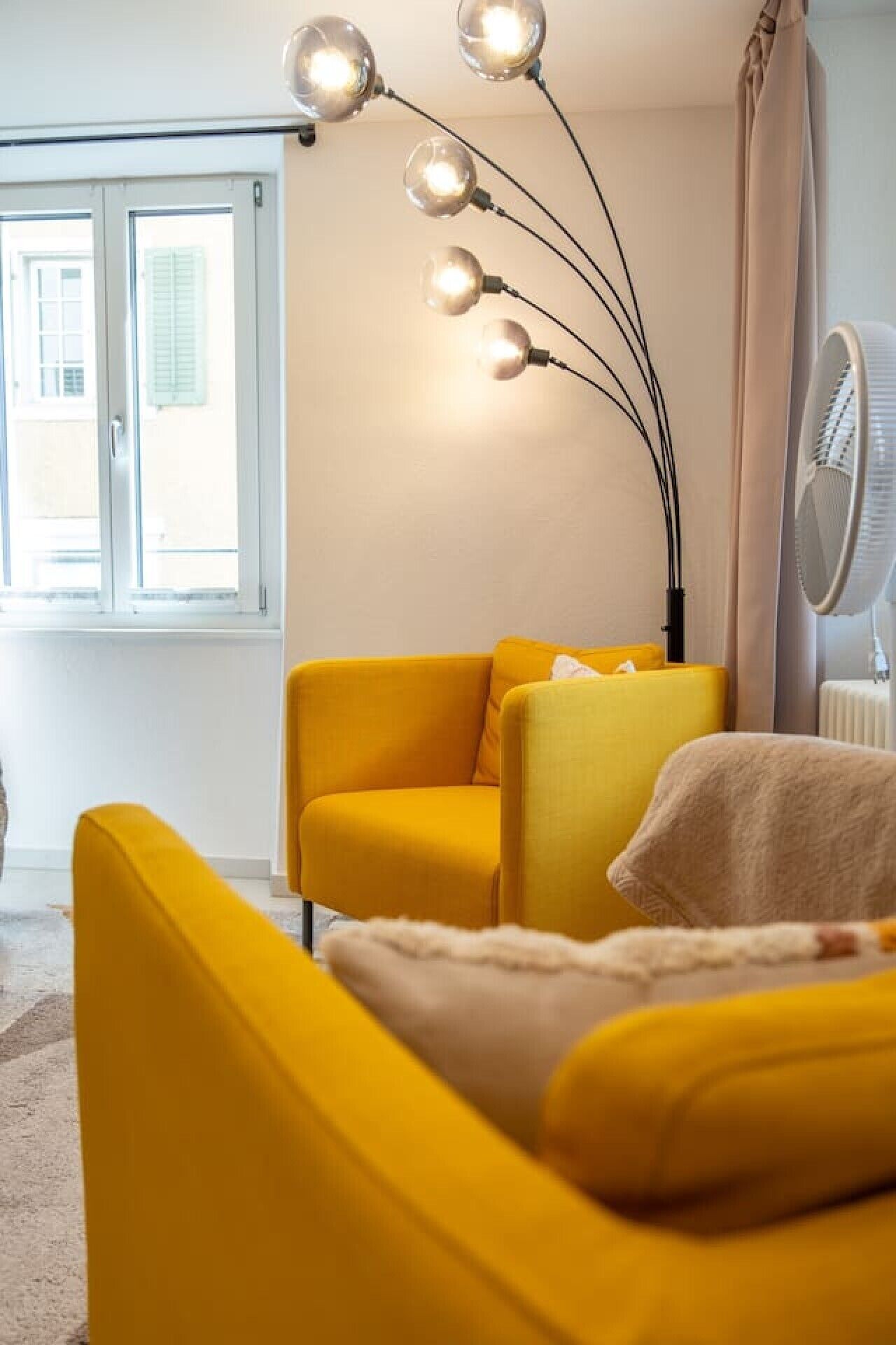 A room with a yellow sofa, a floor lamp, and a window with curtains.