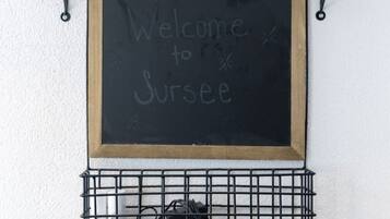 A blackboard with 'Welcome to Surrey' written on it, mounted on a wall with two shelves above and a wire basket below.
