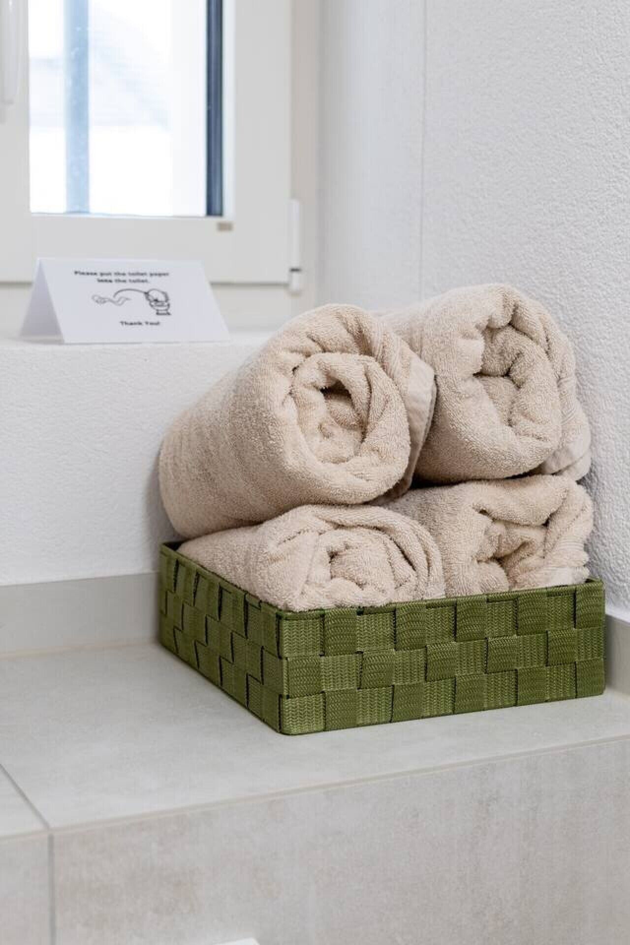 A stack of beige towels in a woven basket on a white shelf.