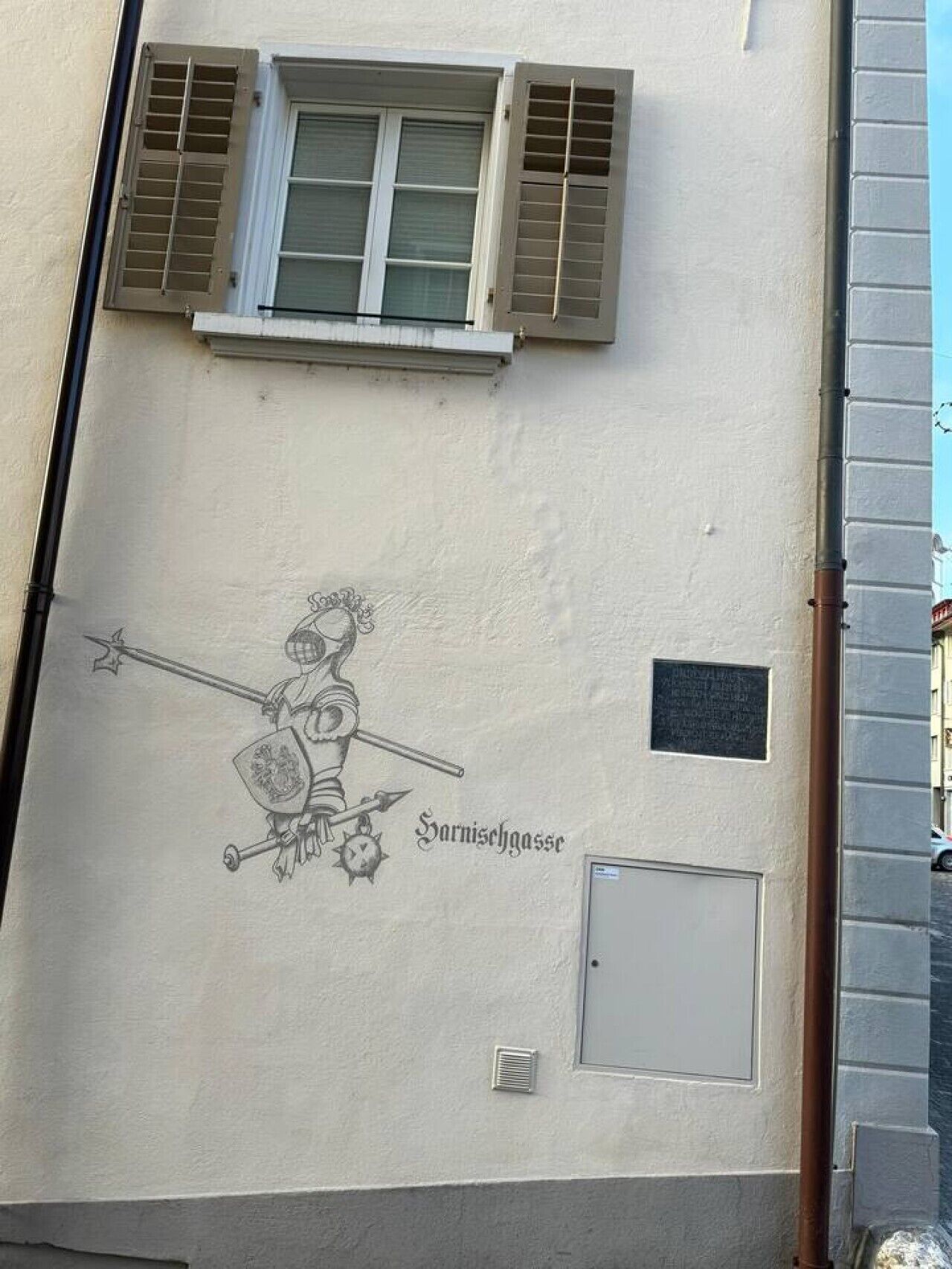 A building facade with a mural of a knight, a window with shutters, and a small plaque.