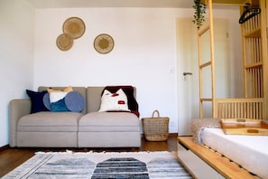 A modern living room with a sofa, a small wooden table, a woven basket, and a wall-mounted decorative item. - Spacious apartment with a view—parking, fully equipped (Huttwil)