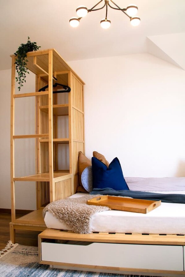 A bedroom with a wooden bed frame, a built-in bookshelf, a hanging plant, and a ceiling light fixture.