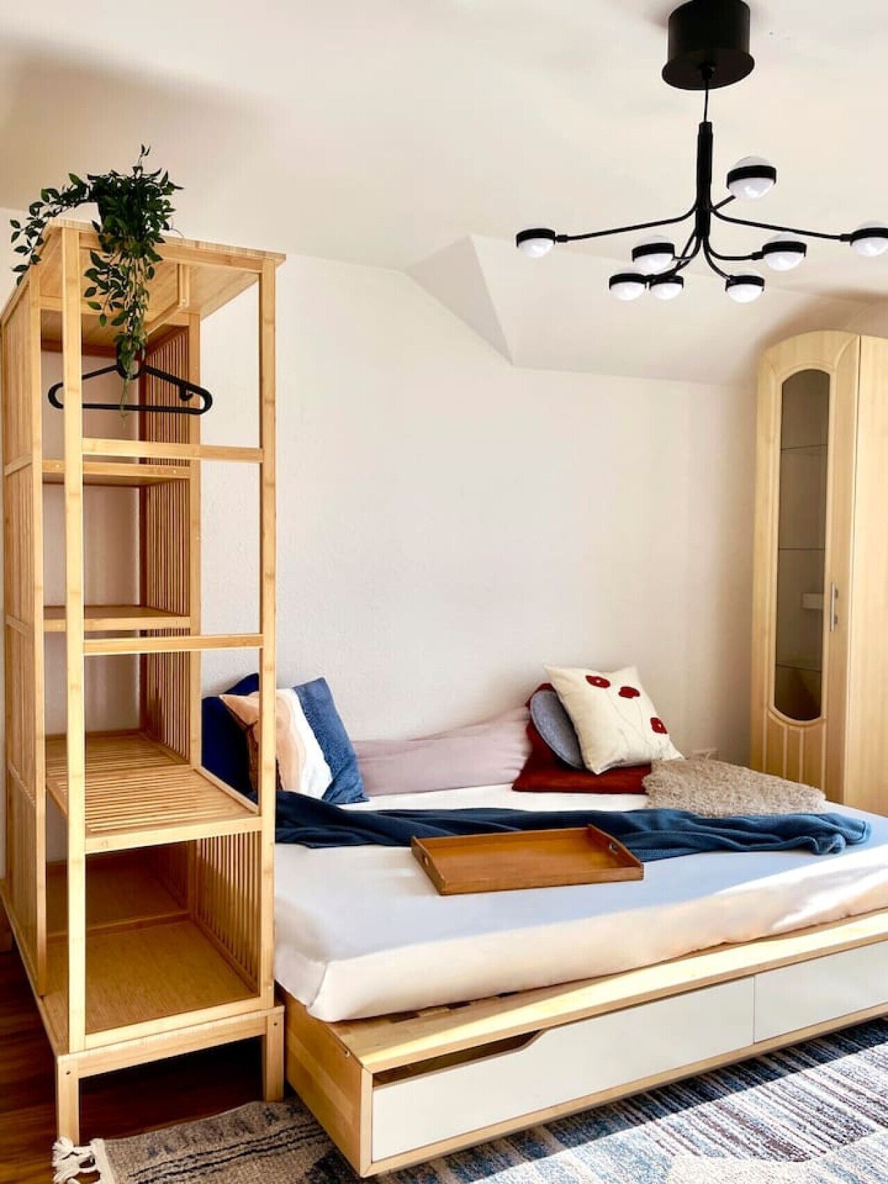 Um quarto com cama, guarda-roupa de madeira, planta pendente e luminária no teto.
