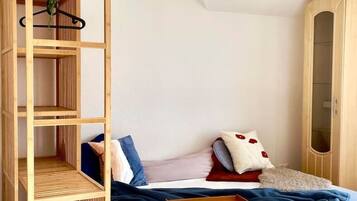 Um quarto com cama, guarda-roupa de madeira, planta pendente e luminária no teto.