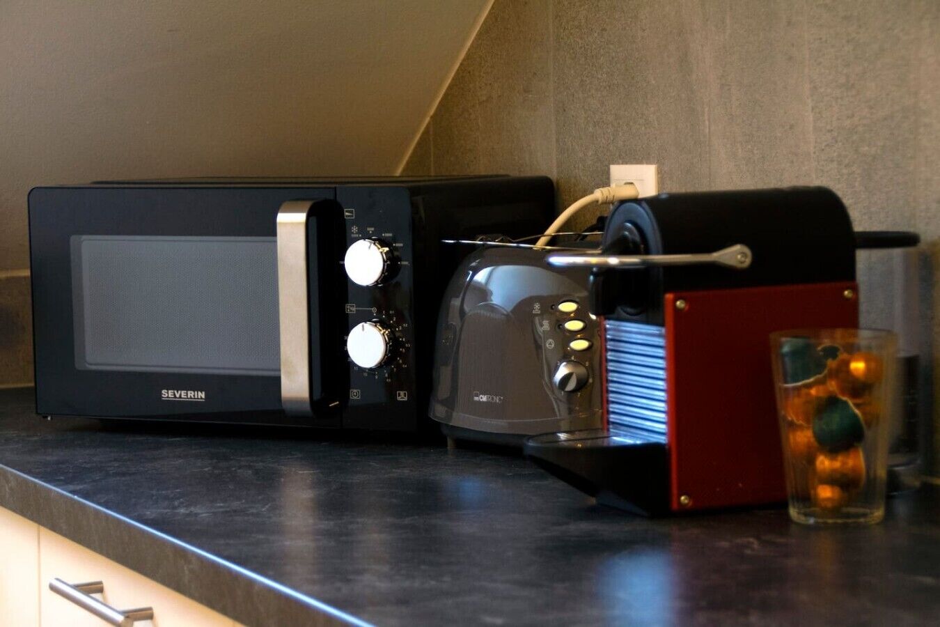 Een keuken met een magnetron, broodrooster en een glas water op het aanrecht.