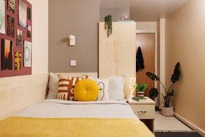 A neatly arranged bedroom with a bed, bedside table, and a wall-mounted shelf. - Student Only The Tannery Leeds (Leeds)