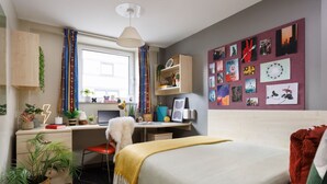Ein Schlafzimmer mit einem Bett, einem Schreibtisch, einem Stuhl, einem Fenster und einer mit Bildern dekorierten Wand.