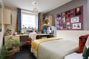 A bedroom with a bed, a desk, a chair, a window, and a wall decorated with pictures. - Student Only The Tannery Leeds (Leeds)