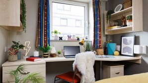 Ein modernes Schlafzimmer mit Schreibtisch, Stuhl, Bett und einem Fenster mit Vorhängen.