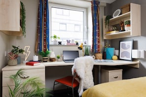A modern bedroom with a desk, a chair, a bed, and a window with curtains. - Student Only The Tannery Leeds (Leeds)