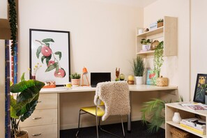 A well-organized workspace with a desk, chair, computer, and various decorative items including plants and a framed picture. - Student Only The Tannery Leeds (Leeds)