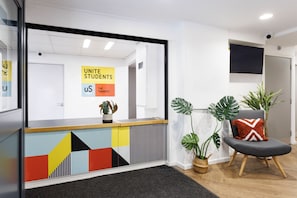 A reception area with a colorful geometric wall design, a potted plant, and a comfortable seating area with a cushion. - Student Only The Tannery Leeds (Leeds)