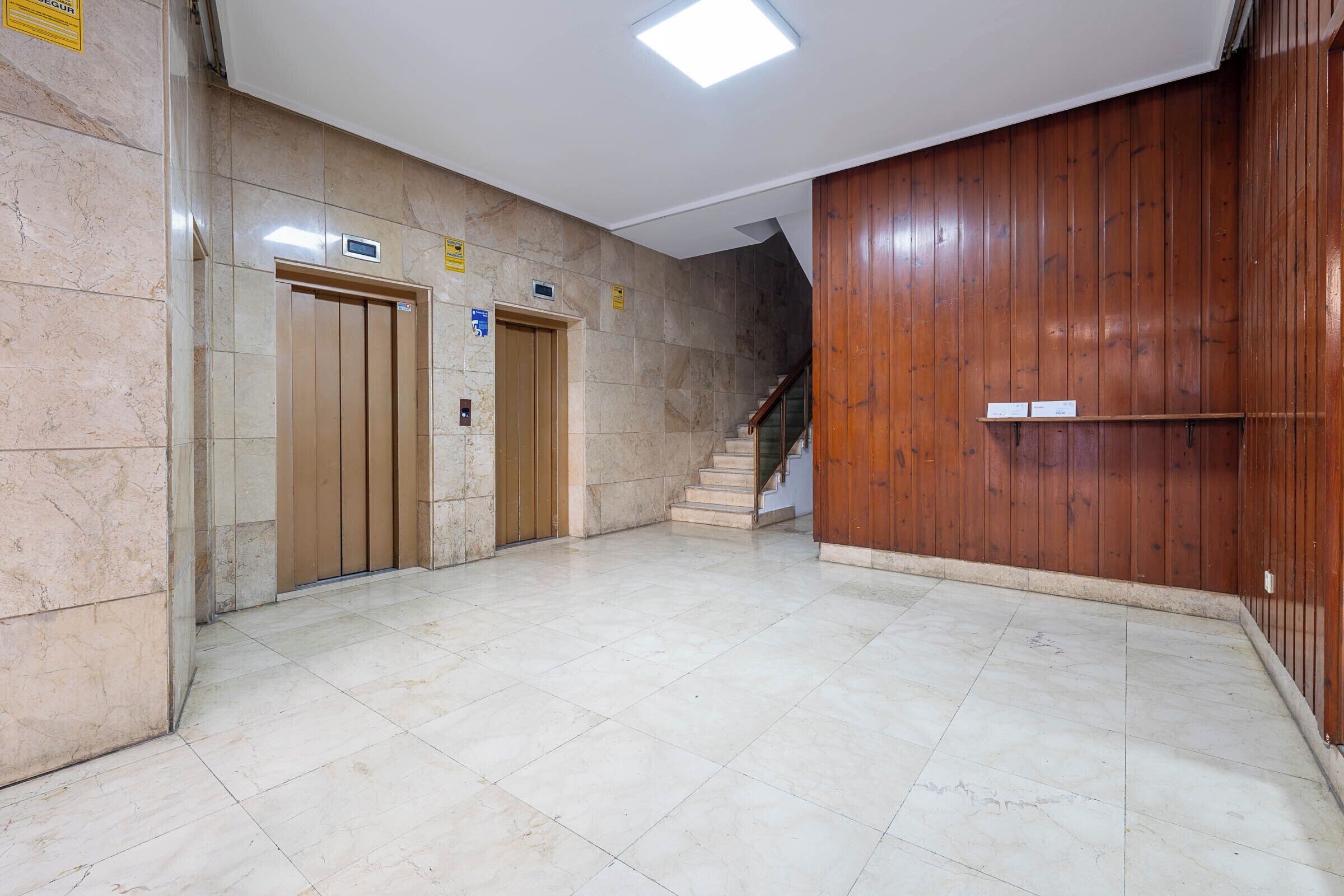A hallway with two elevators, a staircase, and a wooden wall.