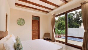 A bedroom with a bed, a chair, a wooden door, and a view of a swimming pool. - The Safari Lodge Pench (Kurai)