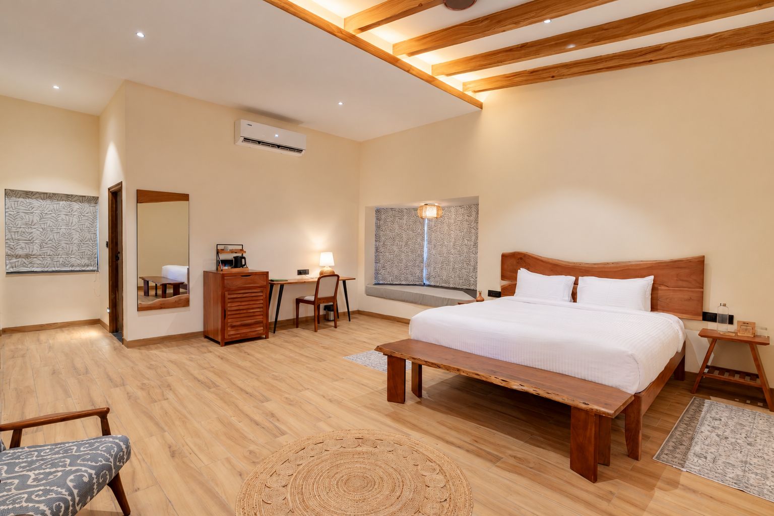 Un dormitorio con una cama de madera, un escritorio, una silla, un aparador y una ventana con cortinas estampadas.