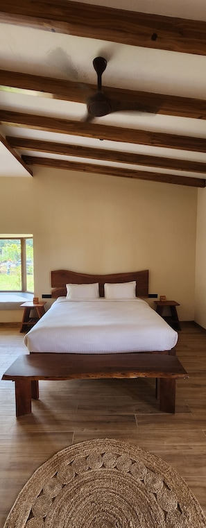 Una habitación con una cama grande, vigas de madera, un ventilador de techo y vistas al exterior.