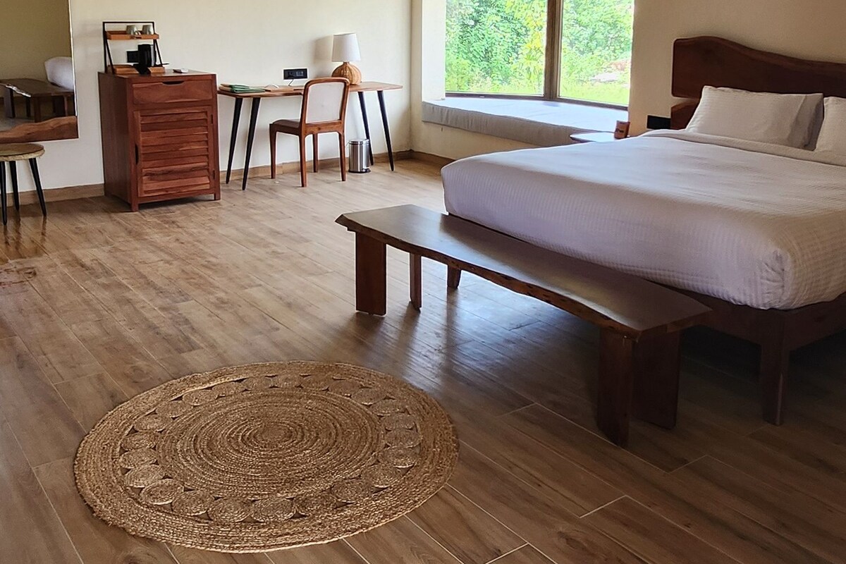 Una habitación con una cama, un escritorio, una silla, un aparador de madera y un ventanal grande.