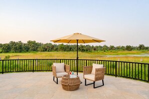 A terrace with two wicker chairs, a round table, and a large umbrella. - The Safari Lodge Pench (Kurai)