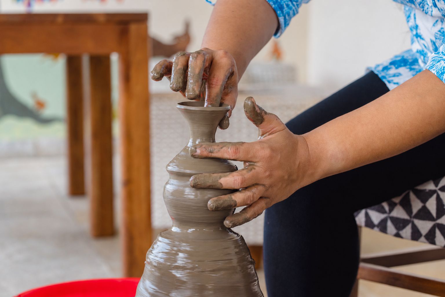 A person shaping a clay pot on a pottery wheel.