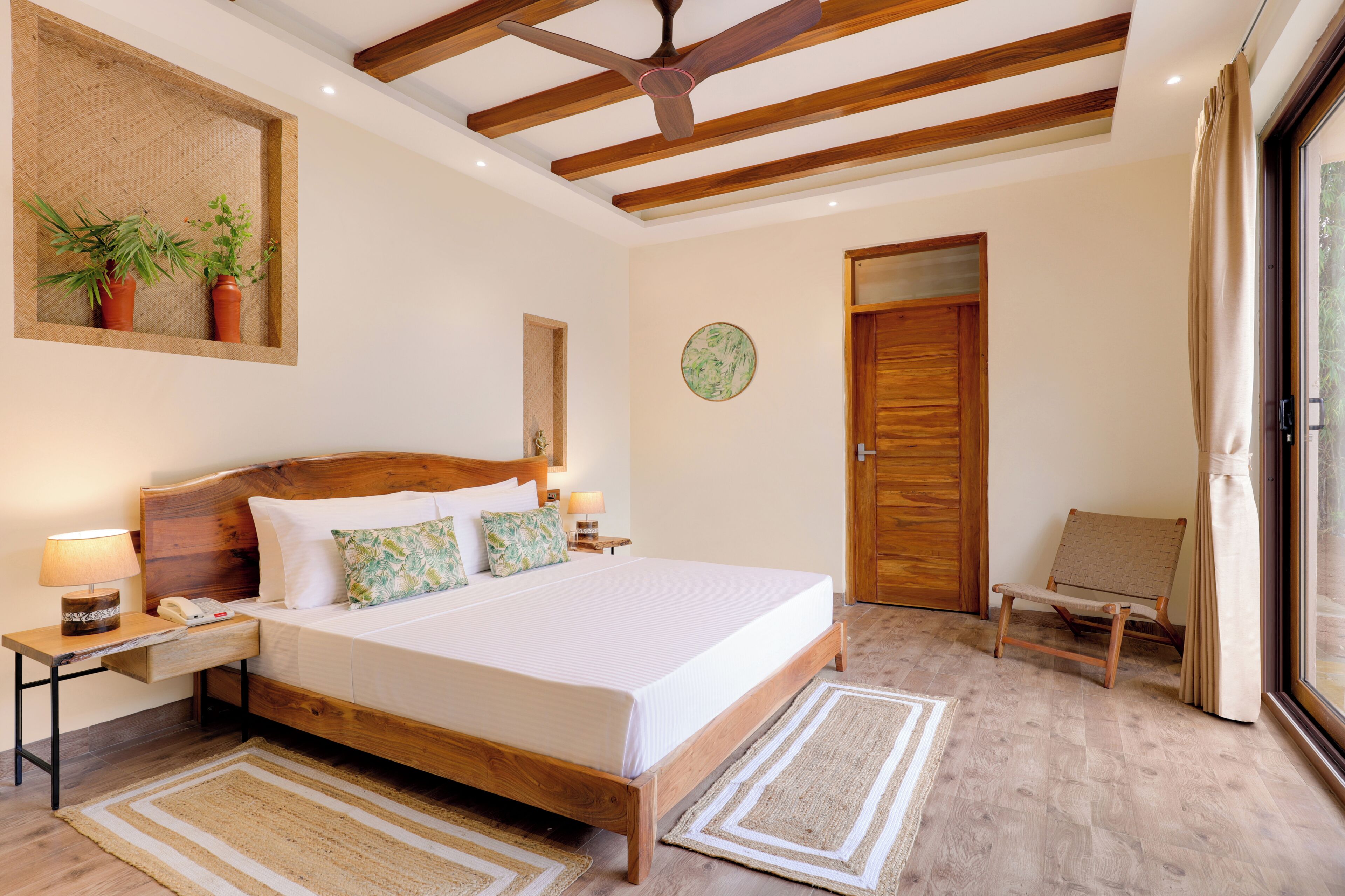 Un dormitorio con una cama de madera, un ventilador de techo, una mesita de noche con lámpara, una silla y una puerta.