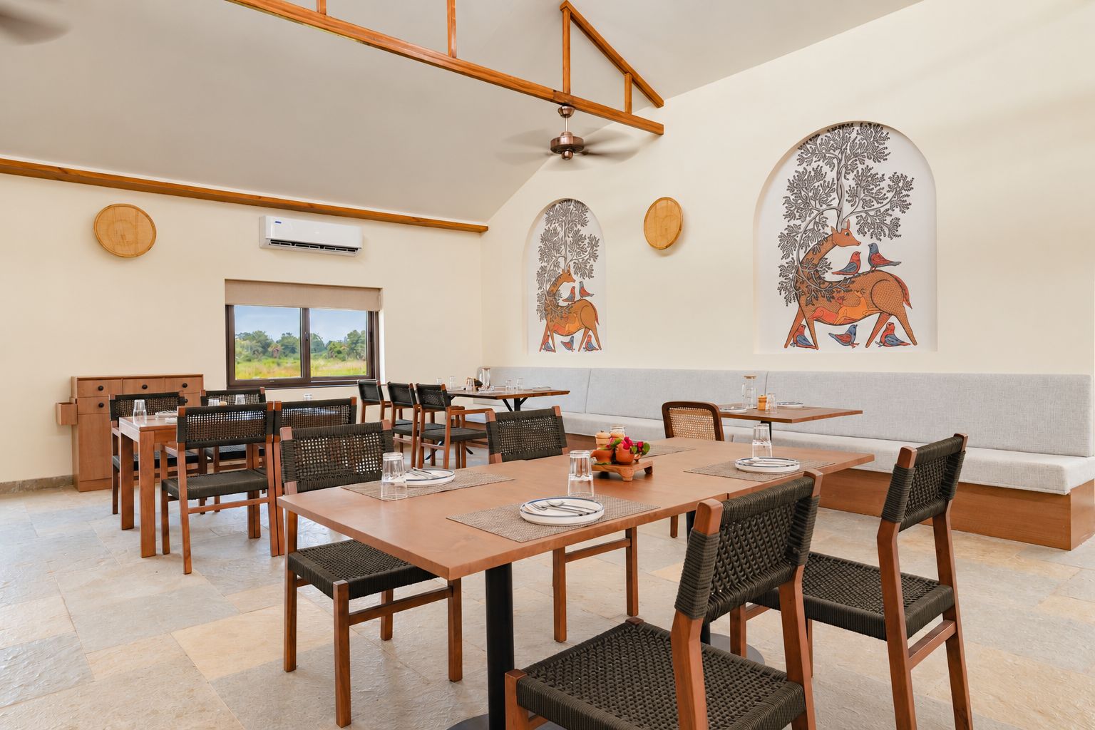 Comedor con mesas y sillas de madera, un ventilador de techo y cuadros con imágenes de animales.