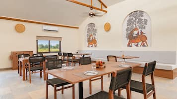 Comedor con mesas y sillas de madera, un ventilador de techo y cuadros con imágenes de animales.