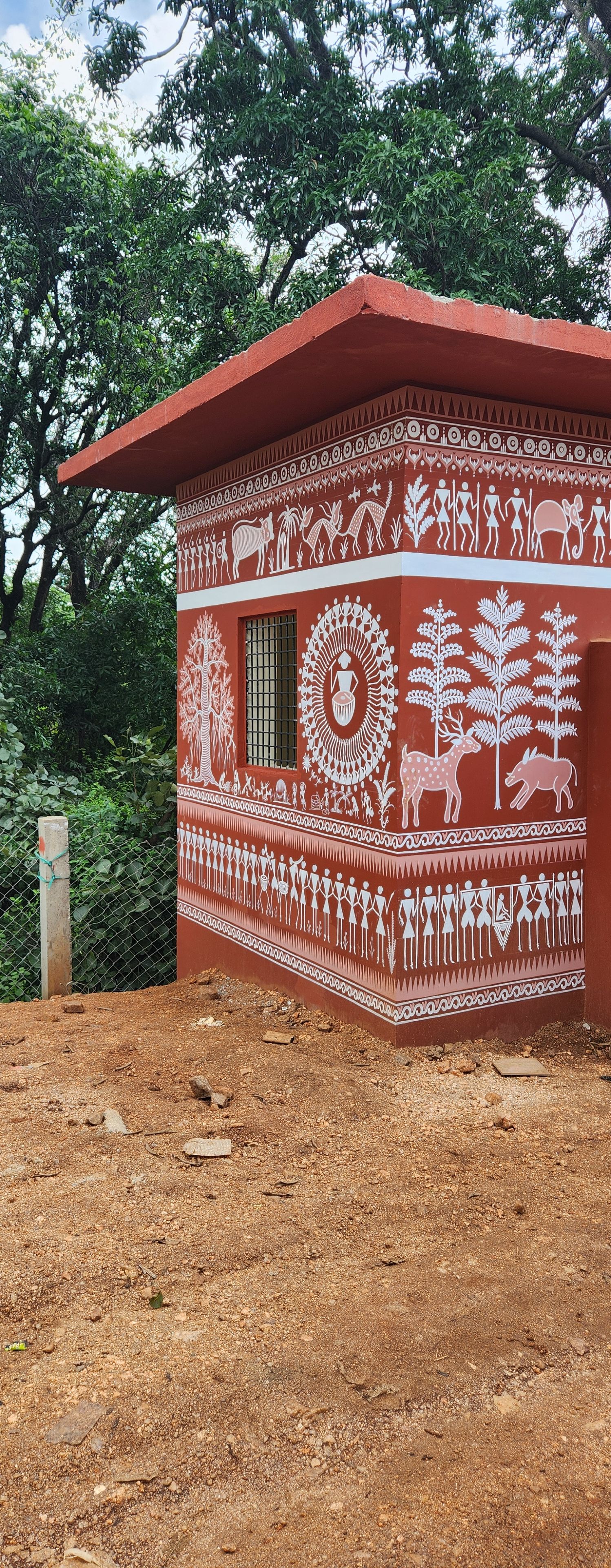 A building with traditional red and white wall paintings, a window, and a dirt ground.