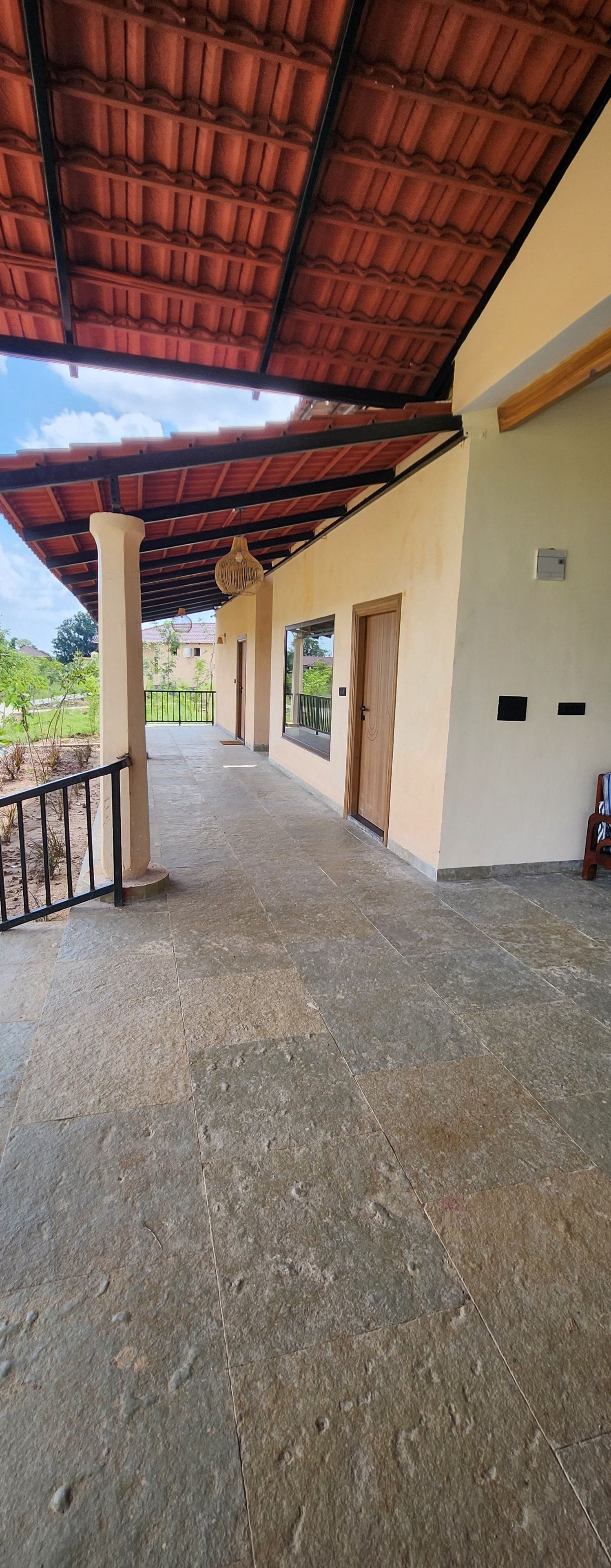 Un espacio al aire libre techado con piso de baldosas, una puerta de madera y una baranda metálica.