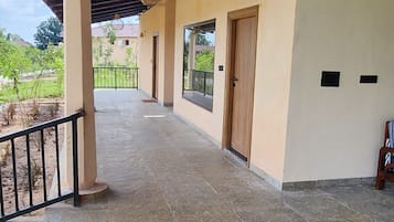 Un espacio al aire libre techado con piso de baldosas, una puerta de madera y una baranda metálica.
