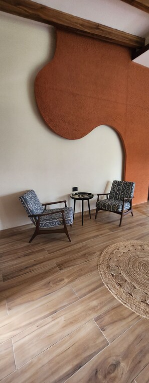 Una habitación con piso de madera, dos sillones con estampado, una mesita redonda y una decoración de pared abstracta de gran tamaño.
