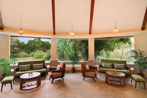 Amplia habitación con techo alto, vigas de madera y grandes ventanales con vistas a un exuberante jardín.