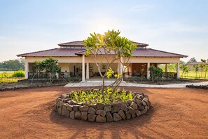 A two-story house with a tiled roof, a covered porch, and a landscaped garden with a central tree. - The Safari Lodge Pench (Kurai)