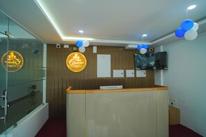 A reception desk with a wooden finish, a glass partition, and a wall-mounted television. - Grace Residency (Sulthan Bathery)