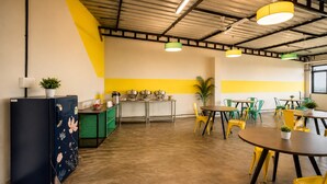 Una cocina moderna con refrigerador, pileta y diversos electrodomésticos. Hay varias mesas y sillas dispuestas para comer.