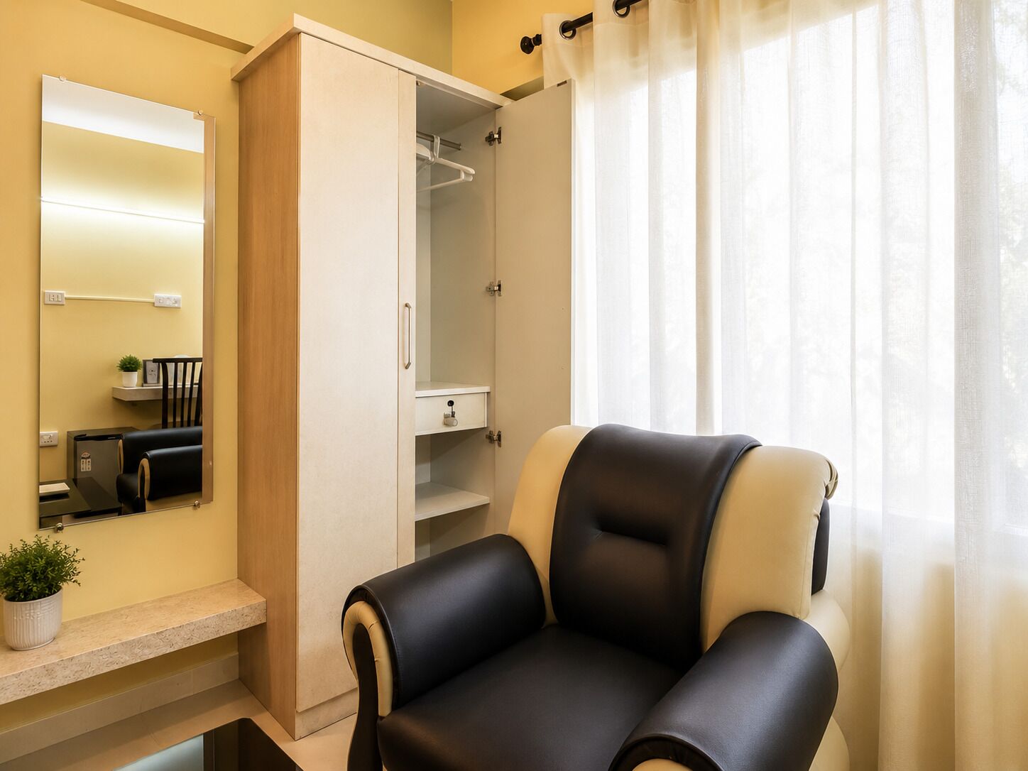 A room with a seating area, a wardrobe, a mirror, and a window with curtains.