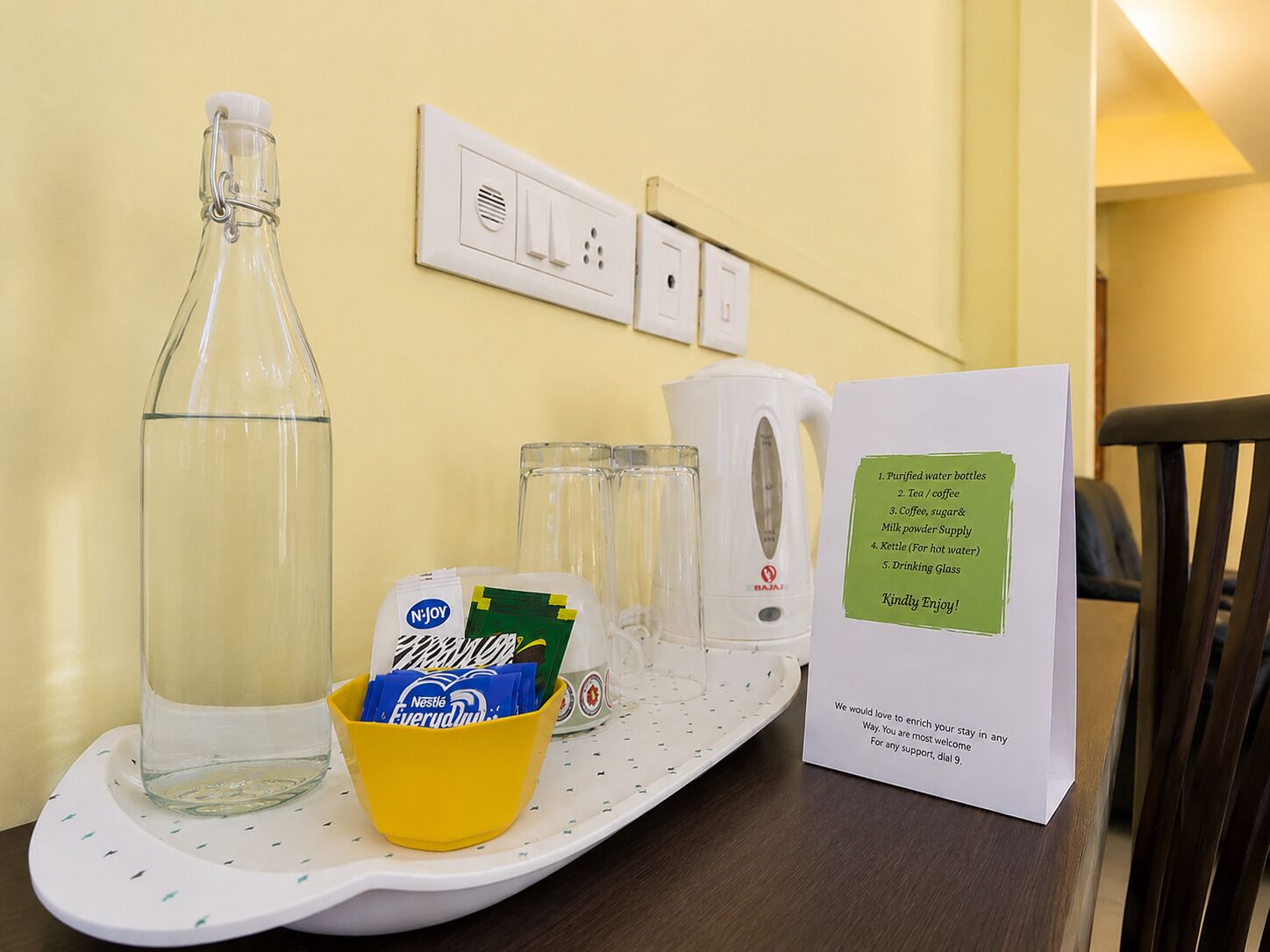 Un plateau contenant une bouteille d’eau, des verres, une bouilloire, un sachet de café Nestlé Everlast et une carte indiquant les équipements disponibles.