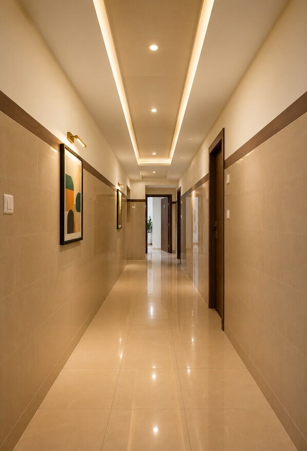 A long, well-lit hallway with a polished floor, doors on both sides, and framed artwork on the walls.