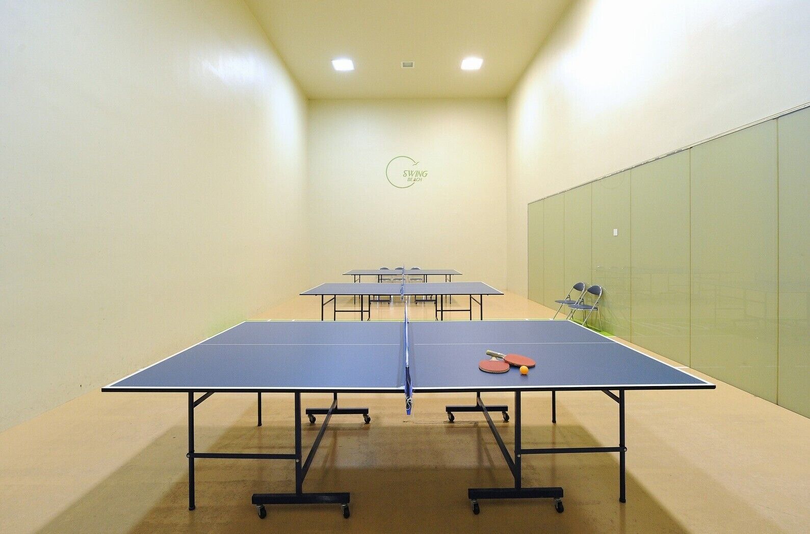 Une pièce équipée de tables de ping-pong, de chaises et ornée d’un logo sur le mur.