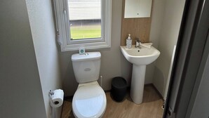 A compact bathroom with a toilet, sink, and window. - Spacious 3-bedroom Mobile Home in Whitley Bay Holiday Park (Whitley Bay)
