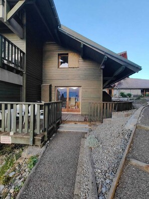 Ein Holzhaus mit Balkon, einer Holzterrasse und einem Kiesweg, der zum Eingang führt.