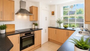 A modern kitchen with wooden cabinets, a black countertop, and a window providing a view of greenery outside. - 2 bedroom property in peaceful Edinburgh location (Edinburgh)