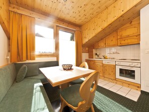 Eine gemütliche Küche mit Holzschränken, einem Esstisch mit Stühlen, einem eingebauten Backofen und einem Fenster mit Vorhängen.