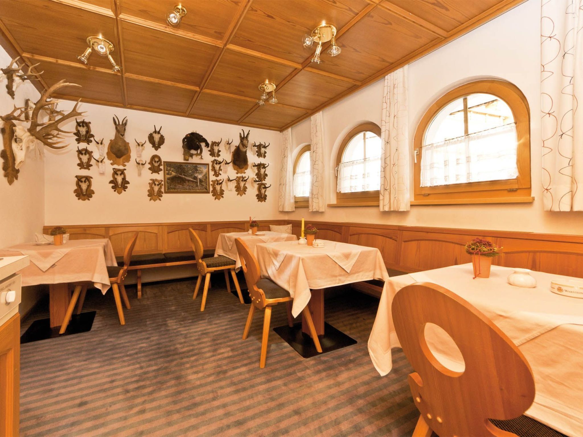 Interior de restaurante con paneles de madera, varias mesas y decoraciones de cabezas de animales colgadas en las paredes.